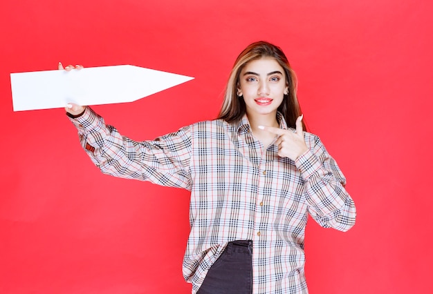 Young woman in checked shirt holding a big arrow pointing to\
the right