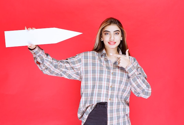 Young woman in checked shirt holding a big arrow pointing to
the right