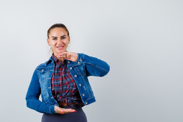 Young woman in checkered shirt, jean jacket pretending to hold something and looking cute , front view