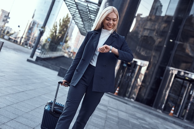 Photo young woman checking her watch and pulling suitcase