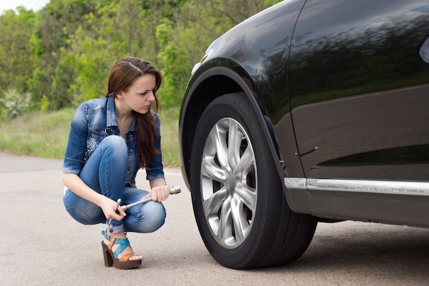 車のパンクしたタイヤをチェックする若い女性