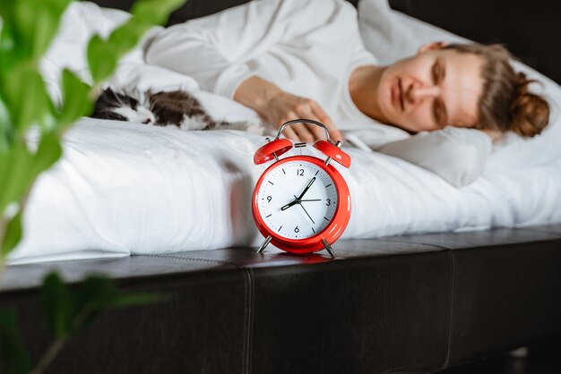 Young woman checking phone with pet cat  at home green plant alarm clock morning time