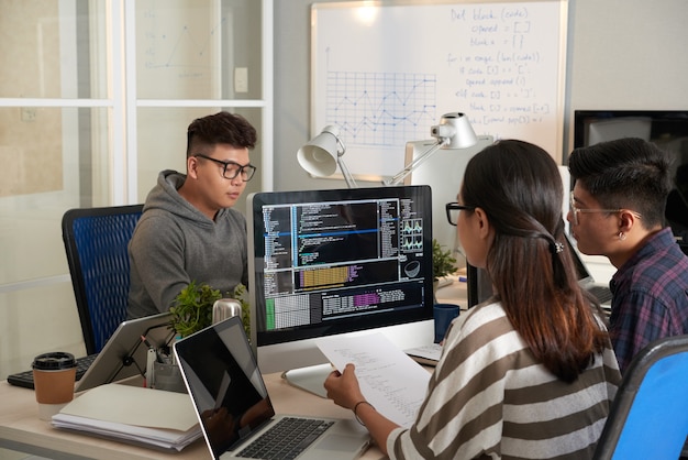 Young woman checking programming code on computer screen and comparing with code on printed document