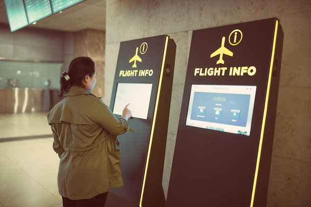 Photo young woman checking time at the flight info kiosk in the airport