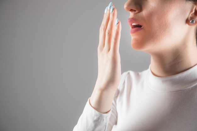 Young woman checks her breath against a gray scene