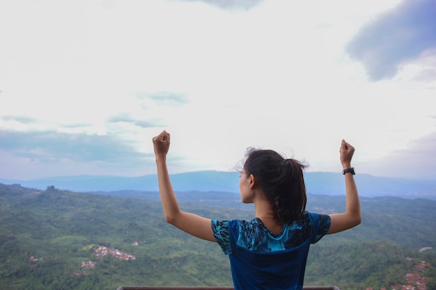 Young woman cheering open arms at mountain peak