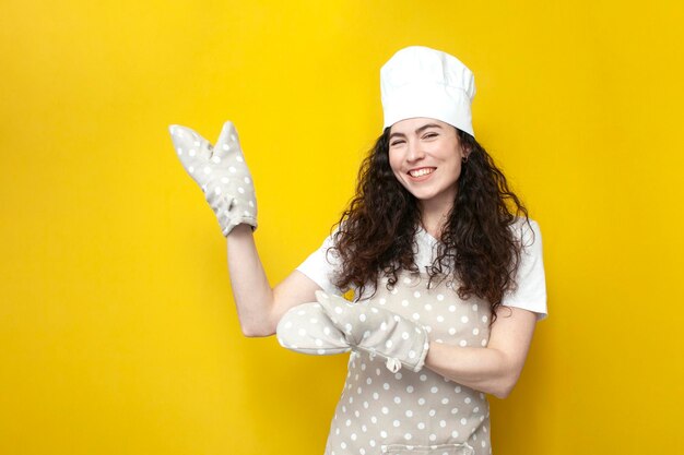 Young woman chef in apron and gloves for baking shows with her hands on copy space