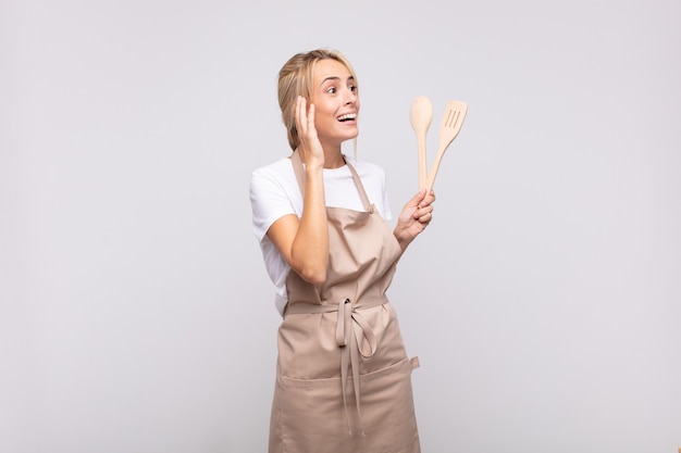 Young woman chef feeling happy, excited and surprised, looking to the side with both hands on face