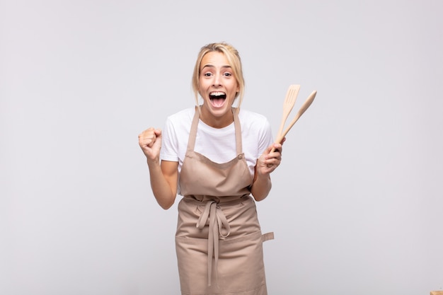 Young woman chef feeling shocked, excited and happy, laughing and celebrating success, saying wow!