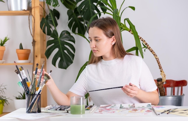 A young woman chooses a brush to paint with watercolor Watercolor drawing on a sheet