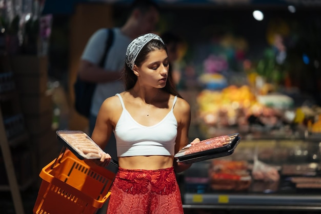 Young woman chooses meat in a grocery store