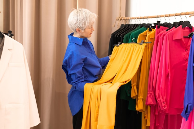 Young woman choosing clothes at store standing at hangers with colorful silk shirts