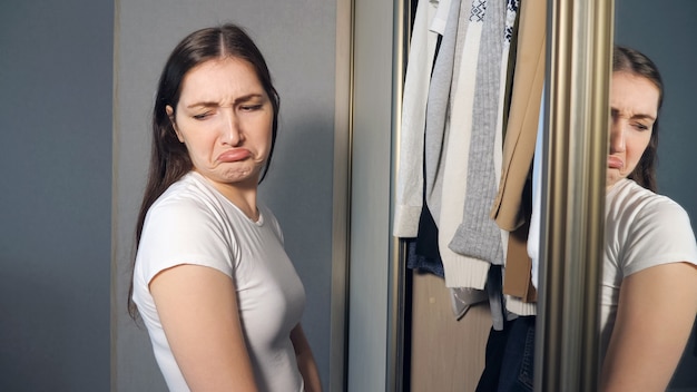 Young woman choosing clothes in wardrobe at home. Nothing to wear concept