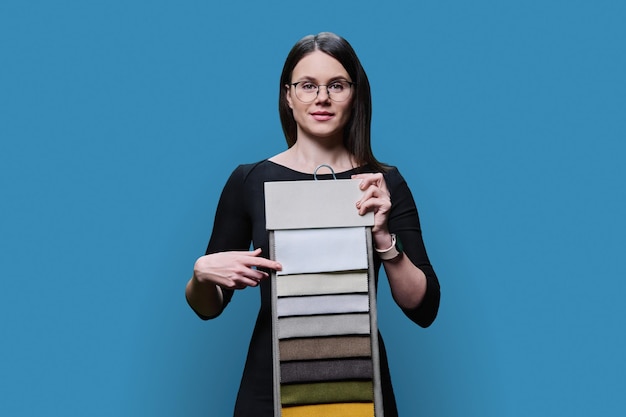 Young woman choosing decorative fabrics for interior on blue background