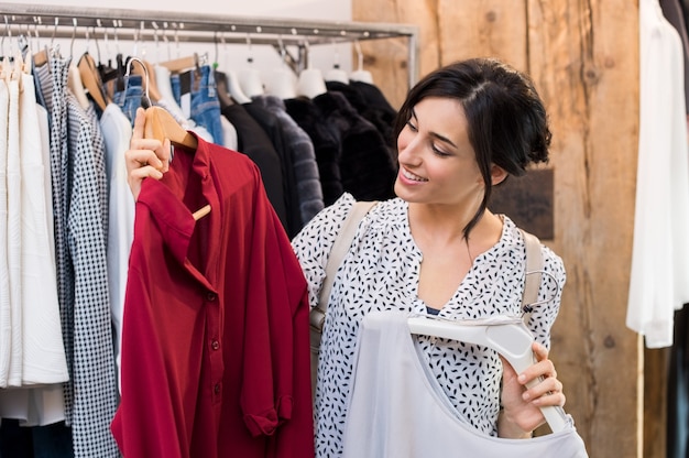 Young woman choosing between dresses in clothing shop