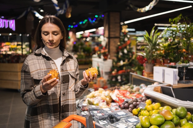 Young woman choosing exotic kiwano fruit in supermarket