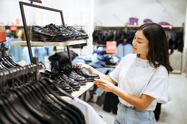 衣料品店で靴を選ぶ若い女性。ファッションブティック、買い物中毒、ブーツを探している買い物客で買い物をする女性