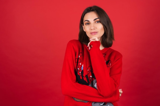 Young woman in a christmas sweater   looks thoughtfully at the camera, hand on chin