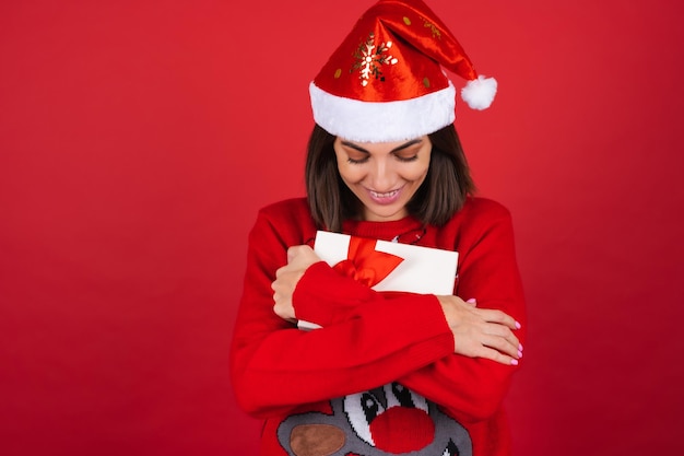 Young woman in a christmas sweater and santa hat   with a gift box  