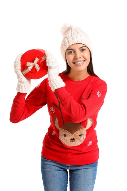 Young woman in christmas sweater and with gift on white surface