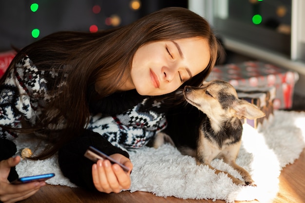 A young woman in a Christmas sweater with a small dog hugs