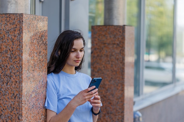 街を歩いている携帯電話でテキスト メッセージを送信する都市の若い女性