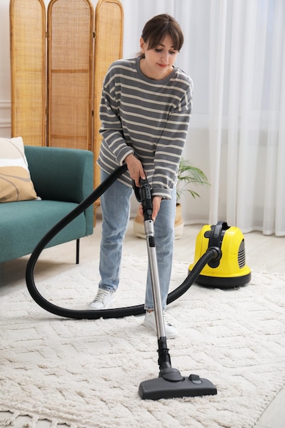 若い女性がリビングで掃除機でカーペットを掃除している