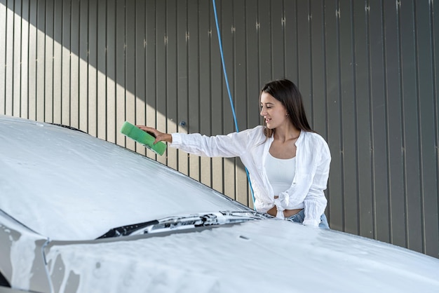 Young woman cleaning her car use foam with a sponge at car wash