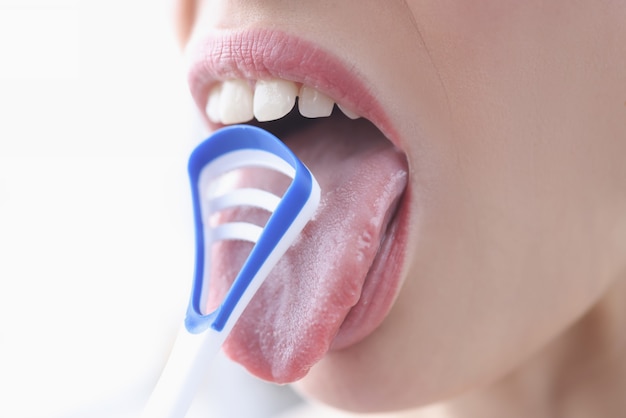 Young woman cleaning her tongue with scraper closeup. Oral hygiene concept