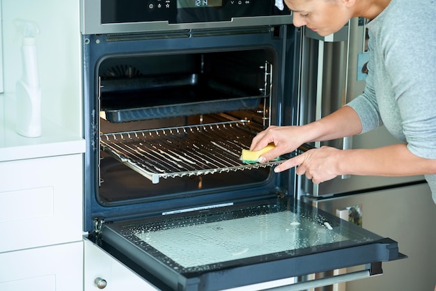 Giovane donna che pulisce il forno in cucina