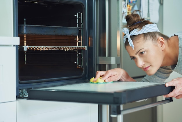 Giovane donna che pulisce il forno in cucina