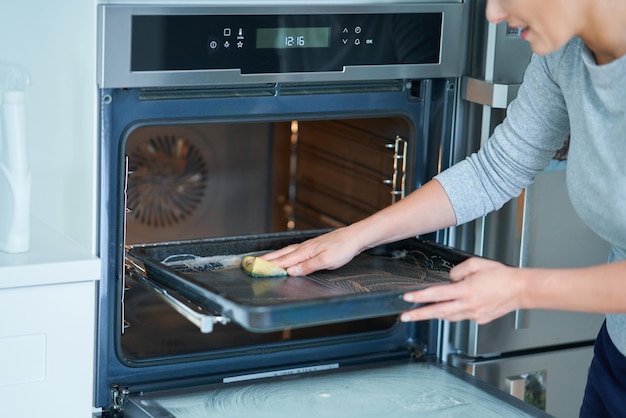 Giovane donna che pulisce il forno in cucina