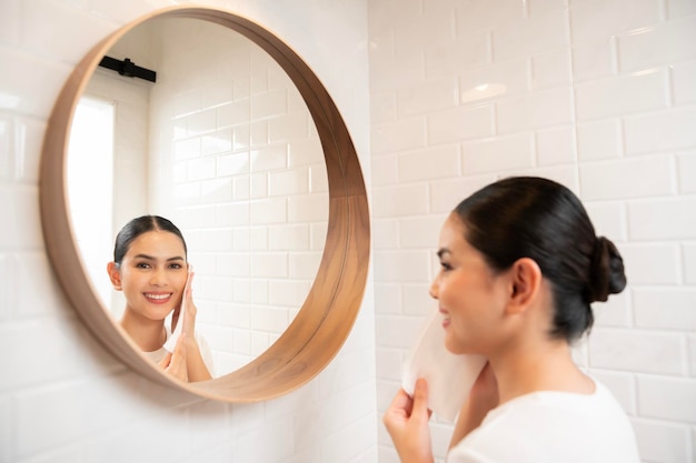 自宅の美容ウェルネス コンセプトでバスルームで彼女の顔にメイクを削除するクリーニングの若い女性