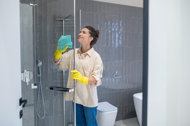 Young woman cleaning the sahower cabin and looking involved