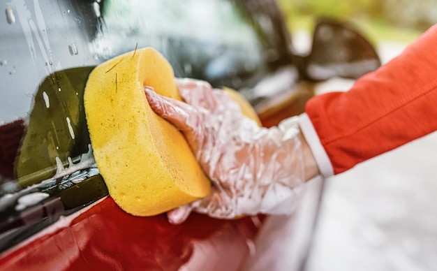 Молодая женщина моет сторону своей машины, деталь крупным планом на руке в перчатке с желтой губкой