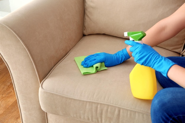 Young woman cleaning sofa with duster closeup