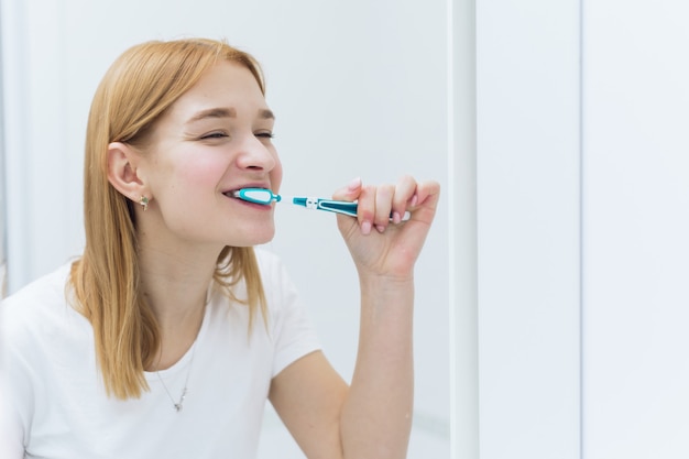Young woman cleaning teeth with toothbrush in bathroom. Oral hygiene.