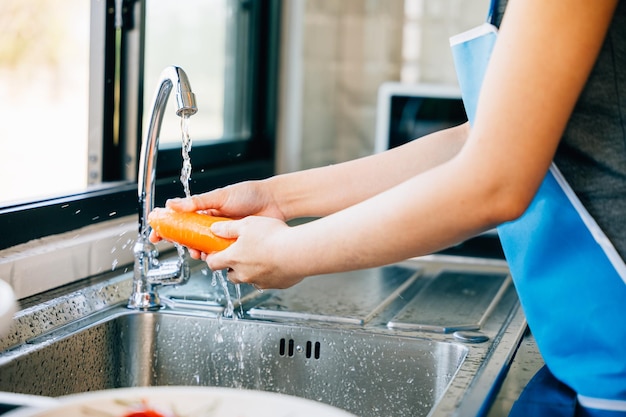 a young woman cleans and washes carrots in the kitchen