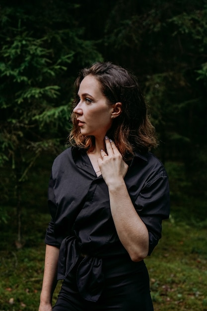 Young woman - close portrait in a dark pine forest. Woman in black shirt