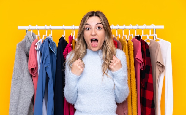 Young woman in a clothing store over isolated yellow wall celebrating a victory