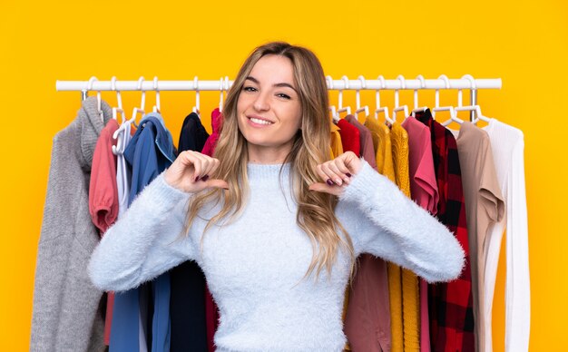 Young woman in a clothing store over isolated yellow wall proud and self-satisfied