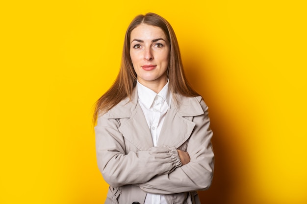 Young woman in a coat crossed her arms over her chest on a yellow background