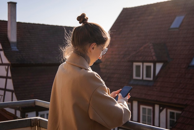 Young woman in a coat with a phone standing on the terrace