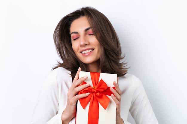 Young woman in a cocktail dress gold chain bright spring pink makeup on a white background Holds a gift box for March 8 and smiles cheerfully