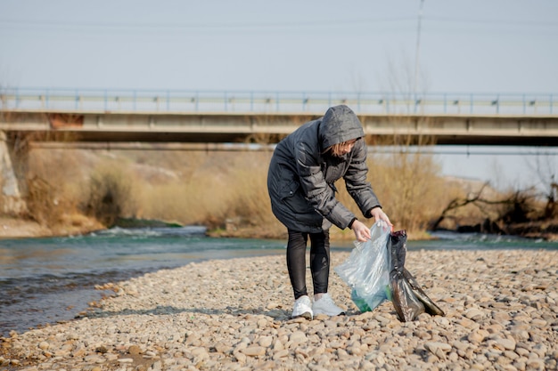 Giovane donna che raccoglie i rifiuti di plastica dalla spiaggia e li mette in sacchetti di plastica neri per riciclarli