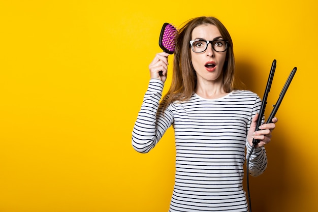 Young woman combing her hair in surprise and keeps curling hair on a yellow background