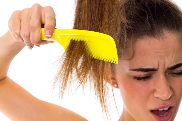 Foto giovane donna che pettina la sua lunga coda di cavallo marrone utilizzando una spazzola per capelli gialla su sfondo bianco in studio