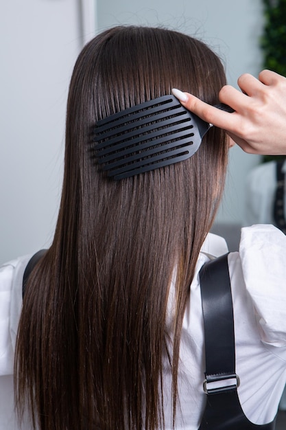 Young woman combing her long dark hair with a comb in a beauty salon.