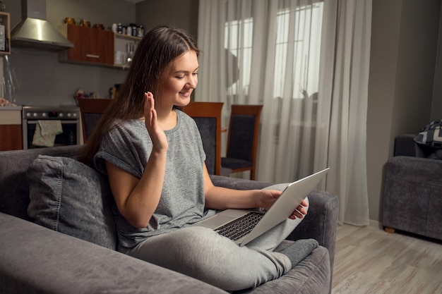 young woman communicates in social networks with laptop, girl sitting at home in chair with laptop, distance learning