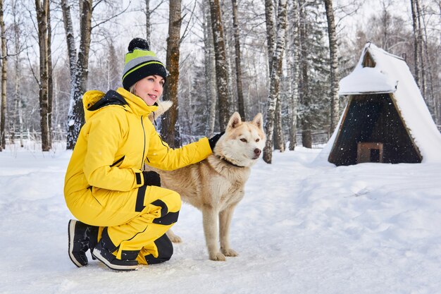 젊은 여자는 겨울 숲에서 허스키 개와 의사 소통합니다
